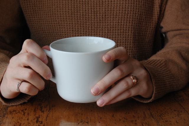 Close up from the front of both hands holding a white cup